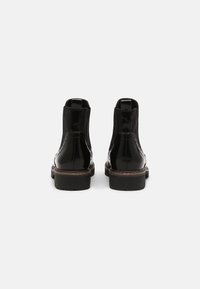 Botas de tobillo de cuero negro con un acabado brillante, paneles laterales elásticos, un distintivo detalle de brogue y suelas resistentes.