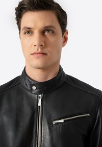 Schwarze Lederjacke mit hohem Kragen, ausgestattet mit silbernen Reißverschlüssen, einer frontalen Tasche mit Reißverschluss und einer glatten Textur.