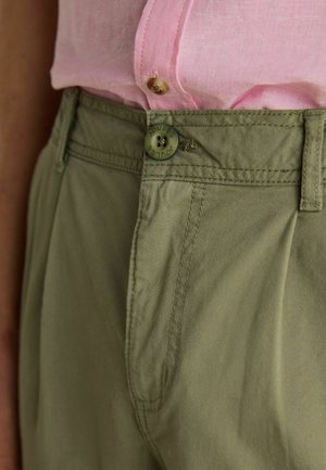 Nahaufnahme von grünem, hoch tailliertem Hosen mit Knopfdetail und einem eingesteckten rosa Hemd, das einen Knopf und die Stoffstruktur zeigt.