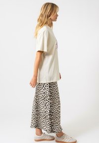 T-shirt beige oversize avec un graphique violet ; associé à une jupe maxi en imprimé léopard. Des baskets grises complètent le look décontracté.