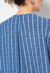Hemd mit blauem Muster, das vertikale Streifen und Blumenmuster zeigt, aus leichtem Stoff gefertigt. Bemerkenswertes Detail mit einer Rückenfalte.