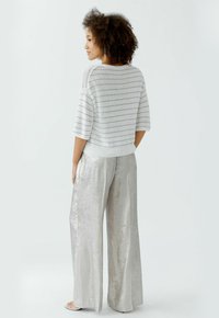Hellgrauer gestreifter Strickpullover mit kurzen Ärmeln, kombiniert mit schimmernden silbernen weiten Hosen. Weiche Textur, lässiges Design und lockere Passform.
