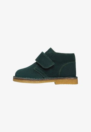 Zapato infantil de ante verde oscuro con una amplia tira de velcro y suela de crepe marrón claro.