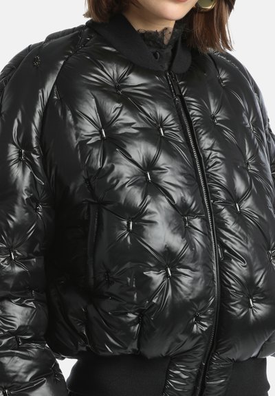 Sort pufferjakke med en glansfuld finish, quiltet design, trykknapkrave og ribbede manchetter. Har sølvdetaljer på syningerne.
