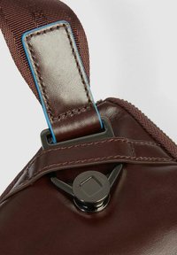 Cintura in pelle marrone con cuciture blu. Presenta un moschettone e un fermo in metallo nero, con una superficie liscia e lucida.