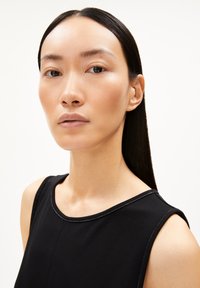 Schwarzes, ärmelloses Top mit rundem Ausschnitt und sichtbaren Nähdetails. Das Modell hat glattes, langes Haar und einen neutralen Teint.