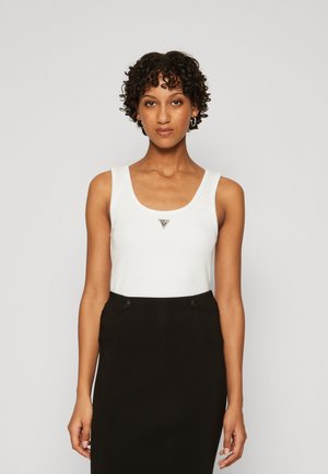 Weißes Tanktop mit quadratischem Ausschnitt, ausgestattet mit einem silbernen Dreieckslogo auf der Brust. Kombiniert mit einem schwarzem, hochgeschnittenen Rock.
