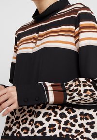 Long-sleeve blouse featuring multicolored horizontal stripes, a black collar, and a leopard print pattern at the hem. Textured fabric with button accents.