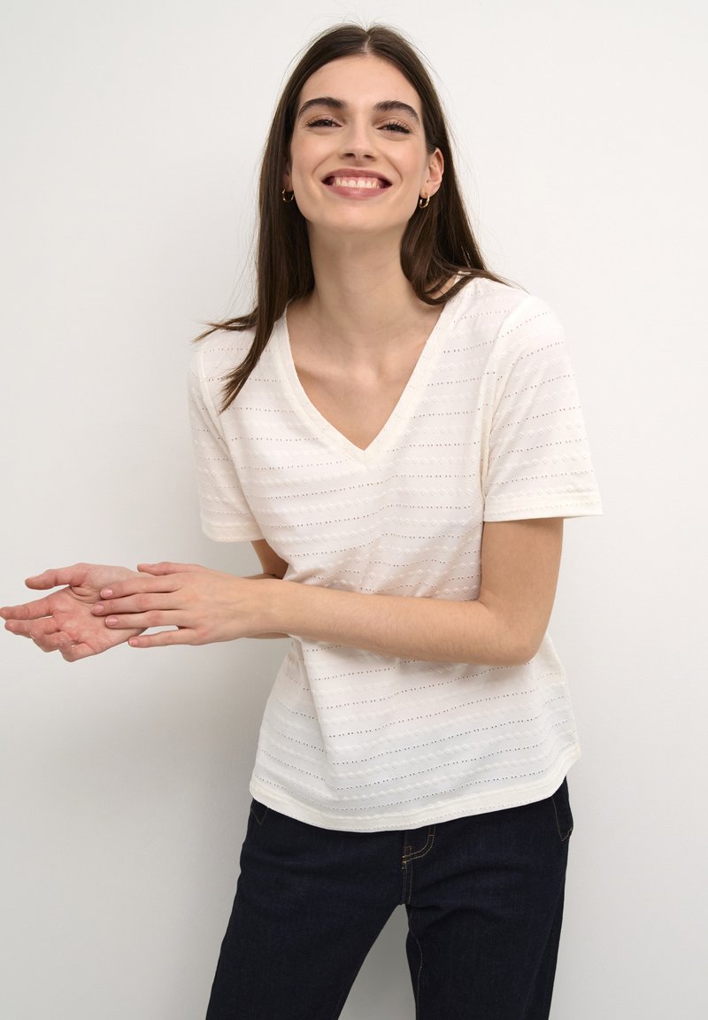 Crème kleurige V-hals t-shirt met korte mouwen, voorzien van gestructureerde strepen en een licht gebogen zoom, gecombineerd met donkere jeans.