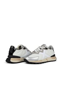 Sneaker bianchi e neri con tomaia in materiale sintetico, accenti argentati e suole testurizzate. Presentano un sistema di chiusura con lacci, colletto imbottito e dettaglio del logo.
