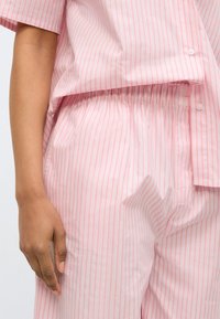 Ροζ ριγέ πιτζάμα δύο τεμαχίων από απαλό ύφασμα. Το πάνω μέρος διαθέτει σχεδιασμό με κουμπιά και άνετη γραμμή, με ελαστική μέσ η στο παντελόνι.