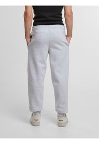 Grijze trainingsbroek met een trekkoord in de taille, zijzakken, een relaxed fit en geribde boorden. G gedragen met witte sneakers.