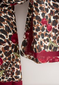 Écharpe imprimé léopard ornée de cerises rouges et de feuilles vertes, fabriquée en tissu léger à la texture douce, bordée d'une bordure bordeaux.