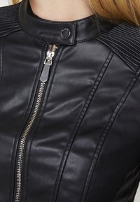 Černá kožená bunda s vysokým límcem, stříbrným zipem a prošívanými detaily na ramenech, která nabízí elegantní a strukturovaný design.