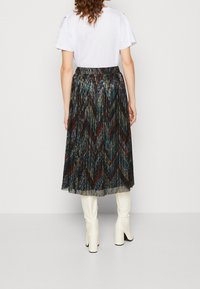 Plisovaná sukně s chevron vzorem v tmavých odstínech a kovovými akcenty. Nositelná nad kolena s elastickým pasem, v kombinaci s bílými botami.