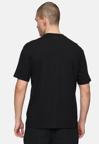 Schwarzes T-Shirt mit kurzen Ärmeln aus Baumwollmaterial, mit Rundhalsausschnitt und dezentem FILA-Logo auf dem Rücken. Schlichtes Design, lockere Passform.