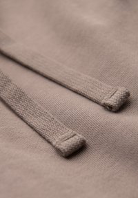 Gros plan de cordons de sweat à capuche beiges montrant la texture tricotée et les extrémités cousues sur un fond de tissu doux.