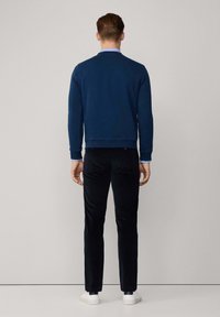 Felpa blu navy con collo alto, polsini e orlo a costine, abbinata a pantaloni neri e scarpe bianche. Tessuto di trama liscia, design minimale.