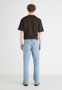Brown short-sleeve t-shirt paired with light blue straight-leg jeans. The jeans feature classic back pockets and a leather patch detail.