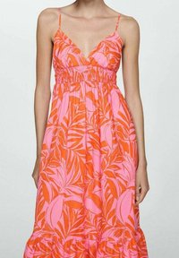 Robe maxi arborant un motif vibrant de feuilles de palmier orange et rose, avec un corsage froncé ajusté et de fines bretelles. Ourlet évasé.