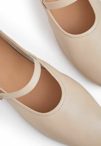 Zapatos de cuero beige con punta redonda y un diseño recortado. Presentan una correa estrecha en la parte frontal y detalles de costura visibles.
