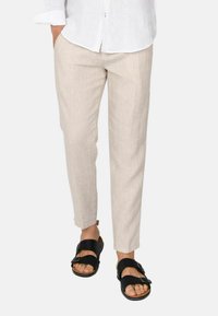 Pantaloni in lino a gamba affusolata color beige chiaro abbinati a sandali neri con due fasce larghe e fibbie, che mettono in evidenza un look estivo rilassato.