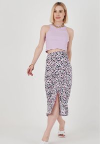 Crop top lilla abbinato a una gonna midi floreale con uno spacco laterale, sandali bianchi, collana a catena e tessuto leggero.