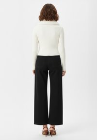 Maglione bianco a coste con collo alto, abbinato a pantaloni neri a gamba larga. L'outfit presenta un design minimalista e una texture del tessuto liscia.