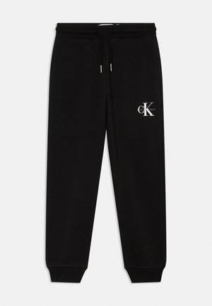 Čierne tepláky s elastickým pásom, sťahovacou šnúrkou a rebrovanými manžetami. Na boku sa nachádza biele logo Calvin Klein. Hladká textura.