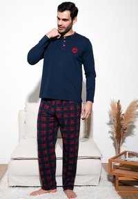 Top de manga larga en color navy con detalles rojos y botones, combinado con pantalones de pijama de cuadros rojos y azules, exhibido en una modelo.