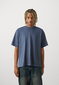 Tricou cu mânecă scurtă, cu gât rotund, din bumbac de culoare albastru închis, croială lejeră, cu un detaliu subtil al logo-ului pe piept. Textură netedă, design minimalist.