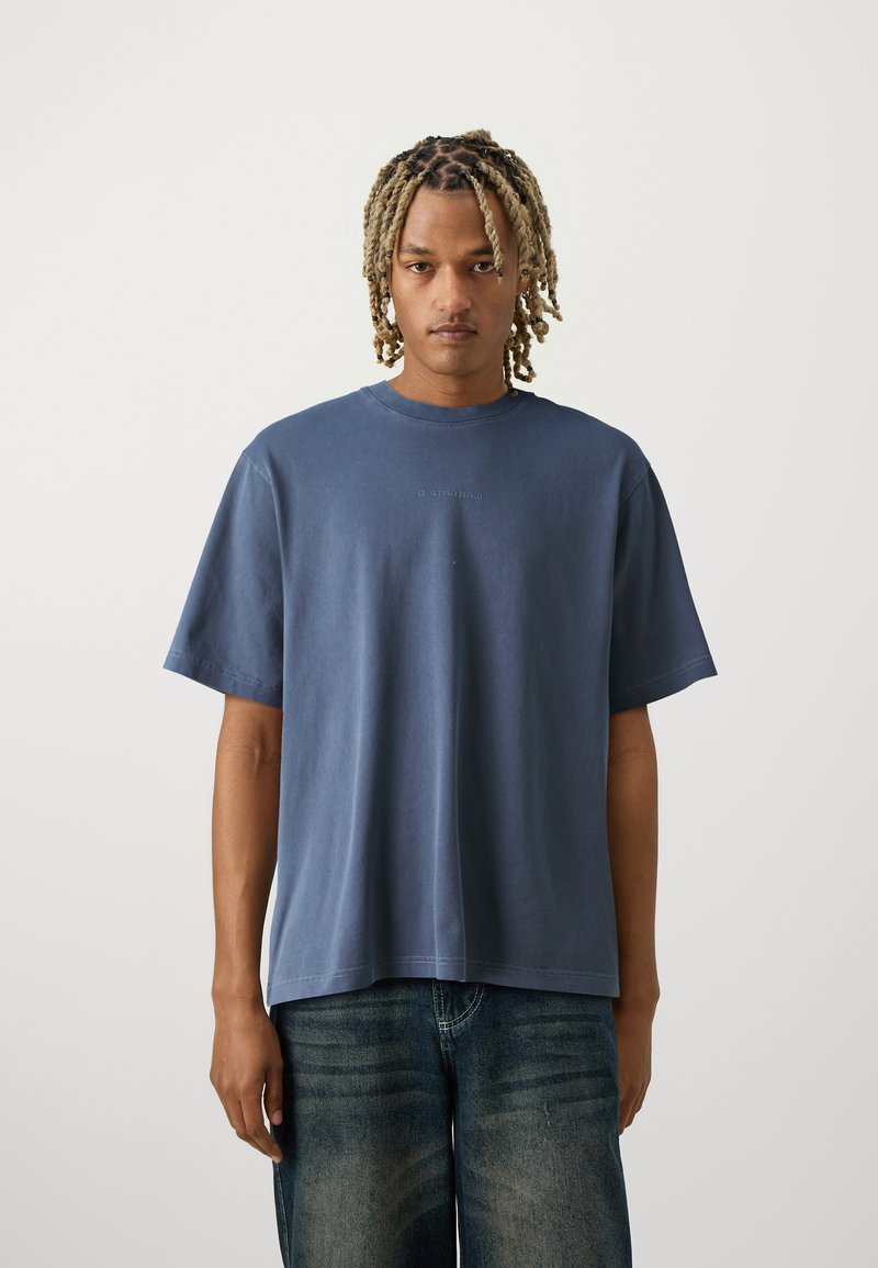 Tricou cu mânecă scurtă, cu gât rotund, din bumbac de culoare albastru închis, croială lejeră, cu un detaliu subtil al logo-ului pe piept. Textură netedă, design minimalist.