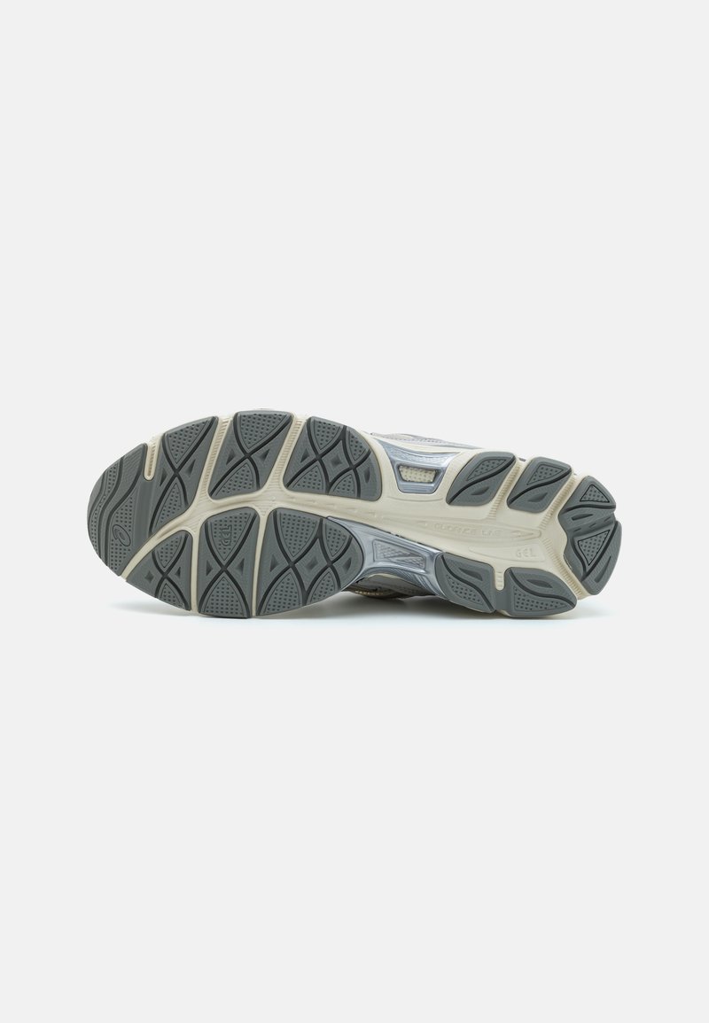 Laufschuhsohle, grauer Gummi mit strukturiertem Profil, akzentuiert durch eine beigen Zwischensohle, ausgestattet mit Flexrillen für verbesserten Grip und Flexibilität.
