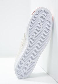 Kermanvärinen tennari, jossa sileä nahkapäällinen, rei'itetyt yksityiskohdat ja aaltoilevaa pintakuviointia esittävä kuvioitu kumipohja.