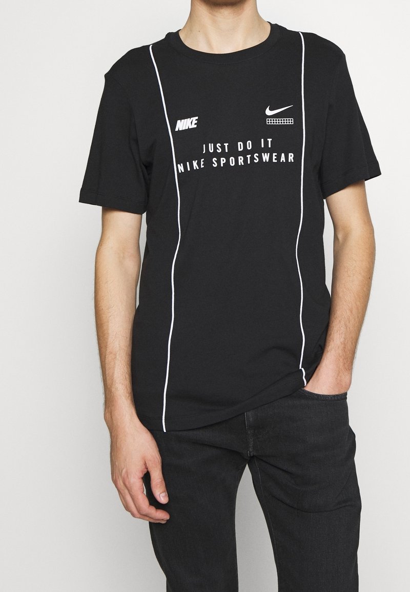 Schwarzes Baumwoll-T-Shirt mit kurzen Ärmeln, weißen Akzenten und Nike-Branding, einschließlich des "Just Do It"-Textes und Logos auf der Vorderseite.