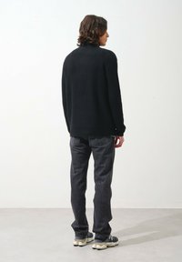 Schwarzer gerippter Pullover mit hohem Kragen, kombiniert mit grauen Jeans. Das Outfit verfügt über Sneaker in neutralen Tönen und einen lässigen Schnitt.