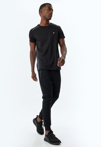 Sort atletisk t-shirt med korte ærmer, med kontrasterende stikninger og et lille logo. Sæt sammen med sorte tapered joggers og sneakers.