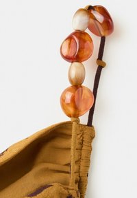 Masque facial en tissu marron avec boucle élastique pour l'oreille décorée de quatre grosses perles brillantes ambre et beige.