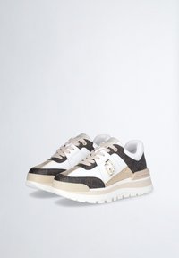 Zapatilla en blanco y negro con un diseño de logotipo texturizado, acentos dorados y una suela blanca gruesa. Cuenta con un cuello acolchado y cordones en beige.