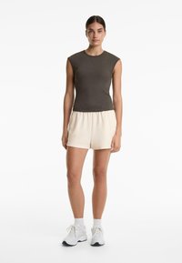 Donkergrijs mouwloos top met een ribbeltextuur, gecombineerd met crèmekleurige shorts, afgewerkt met witte sneakers en enkelsokken.