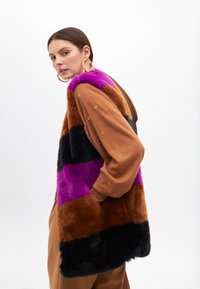 Faux fur vest featuring horizontal stripes in purple, black, brown, and orange-brown. Accented with gold hardware on sleeves.