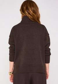 Maglione marrone scuro con colletto alto, polsini e orlo a costine; tessuto in maglia testurizzata; vestibilità rilassata e design con spalla scesa.