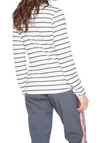 Bluzka z długim rękawem w poziome granatowe i białe paski, wykonana z lekkiego materiału. Połączona z ciemnoszarymi spodniami z różowymi akcentami po bokach.