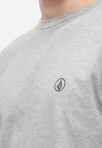 Ανοιχτό γκρι βαμβακερό T-shirt με στρογγυλή λαιμόκοψη και κοντά μανίκια. Διαθέτει μικρό μαύρο λογότυπο στην αριστερή περιοχή του στήθους. Απαλή υφή.