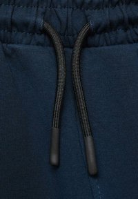 Mörkblå sweatpants med dragsko i midjan. Har svarta snören med gummitips; slät ytstruktur och subtilt ribbad tygmönster.