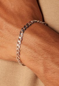 Silver chain bracelet featuring interlocking links, smooth texture, and a polished finish worn on a hand against a beige background.