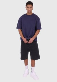 Marineblå, oversized t-skjorte, svarte denimshorts og hvite sneakers. Funksjoner inkluderer en avslappet passform og korte ermer. Enkel design.