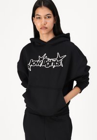 Μαύρο φούτερ κατασκευασμένο από βαμβακερό ύφασμα, με μεγάλο άσπρο λογότυπο σε στυλιζαρισμένη γραμματοσειρά στο μπροστινό μέρος. Χαλαρή εφαρμογή με κουκούλα και τσέπη μπροστά.