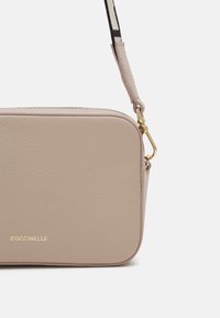 Růžová kožená kabelka přes rameno obdélníkového tvaru s zlatým logem, texturovaným povrchem a odnímatelným popruhem s kontrastním vzorem.