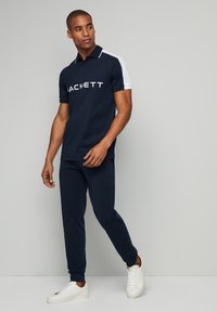 Námornícky polo tričko s bielymi akcentmi, s logom 'Hackett', v kombinácii s vyhovujúcimi jogger nohavicami a bielymi teniskami.